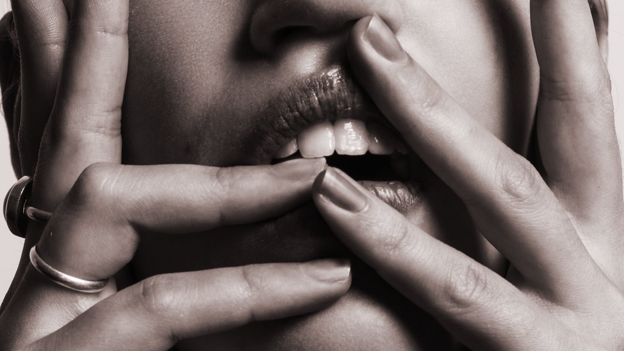 black and white photo of a woman's open mouth with her hands and fingers slightly touching mouth and
